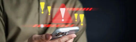 Person hält ein Smartphone unter digitalen Warnsymbolen mit Ausrufezeichen