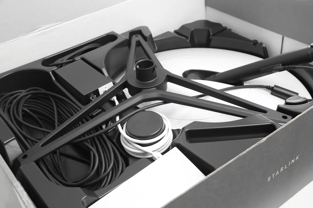 Starlink-Antenne, Standfuß, Kabel und Netzgerät in einem geöffneten Karton.