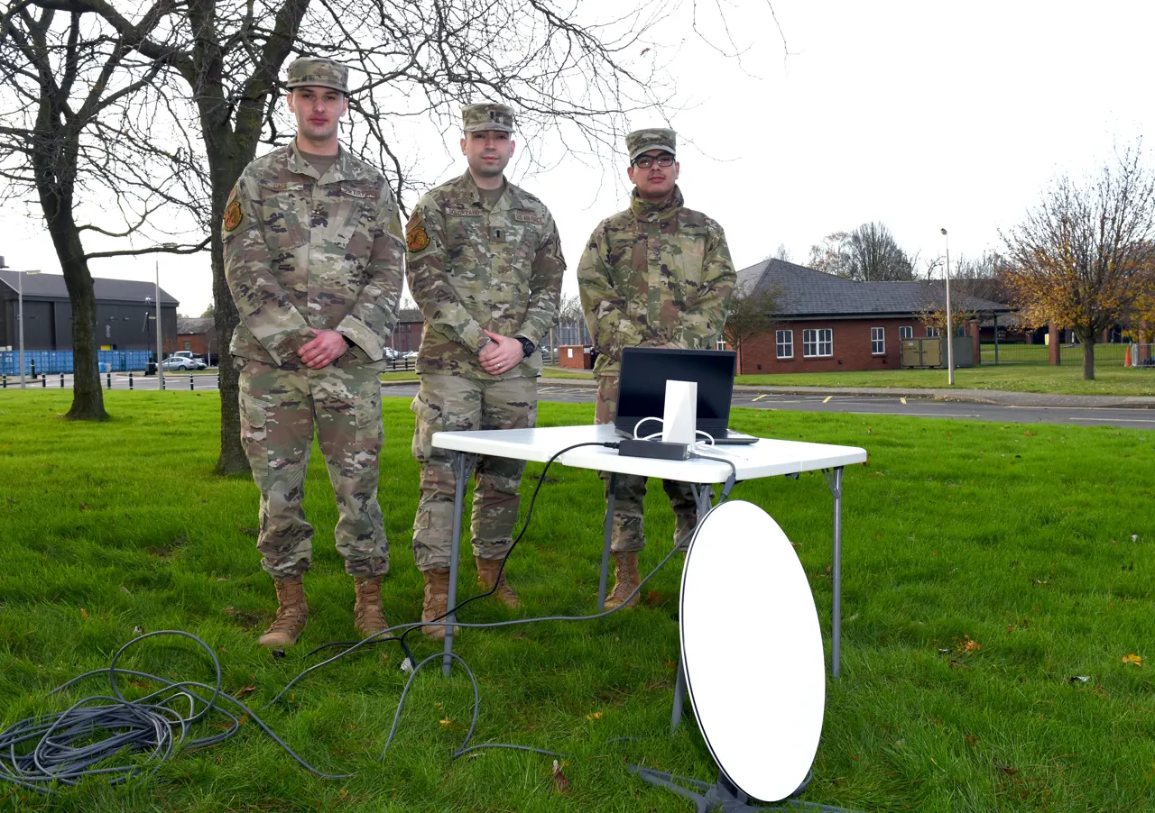 Drei Angehörige der US Air Force stehen hinter einem Tisch mit Laptop und einem Starlink-System.