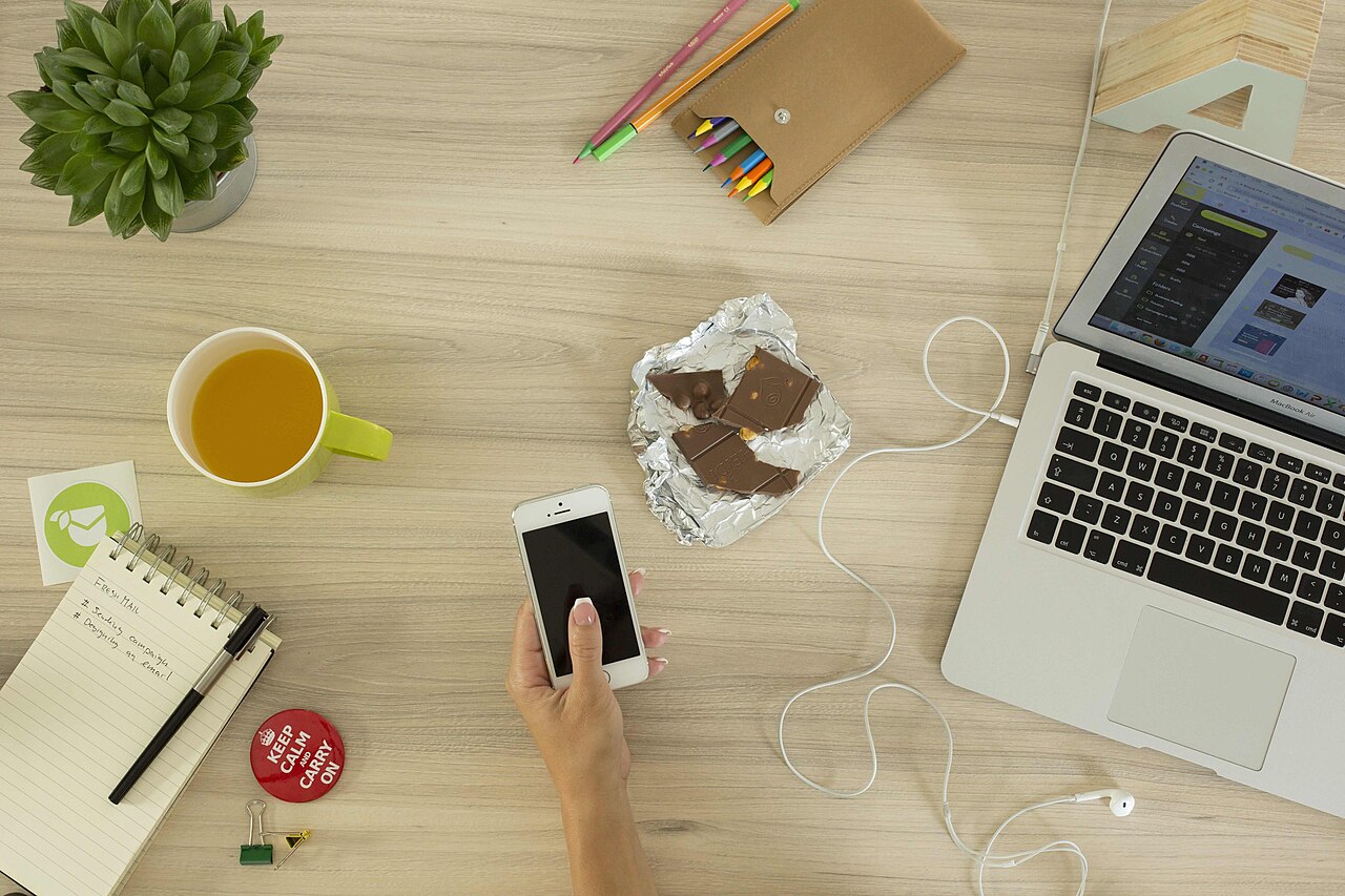 A person holding a smartphone beside an open laptop